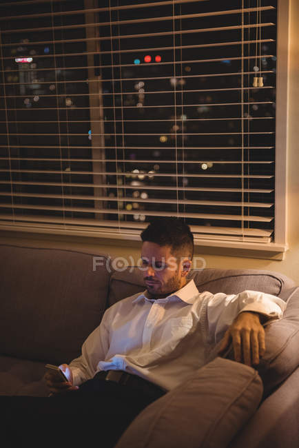 Человек, использующий мобильный телефон в гостиной дома — стоковое фото