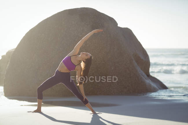 Hermosa mujer realizando ejercicio de estiramiento en la playa en un día soleado - foto de stock