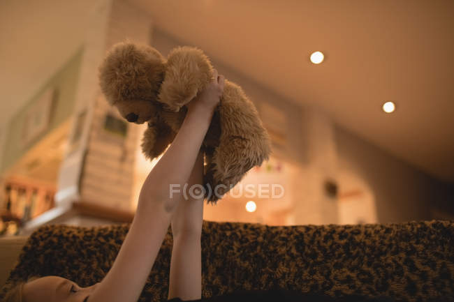 Girl lying on sofa and playing with teddy bear in living room at home — Stock Photo