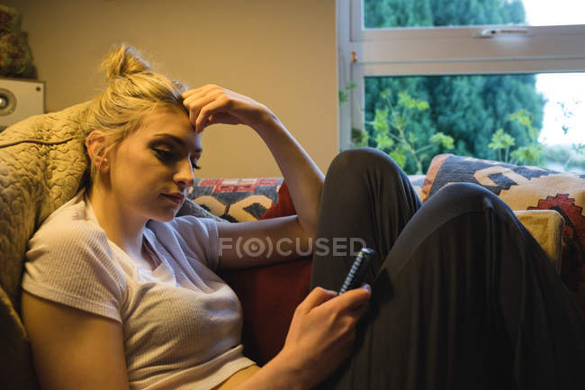 Woman lying and using mobile phone on couch in living room — Stock Photo