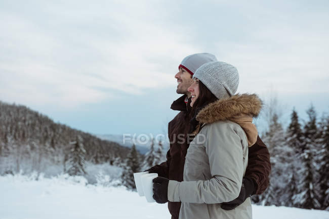 Happy couple standing and holding mug on snow covered mountain — Stock Photo