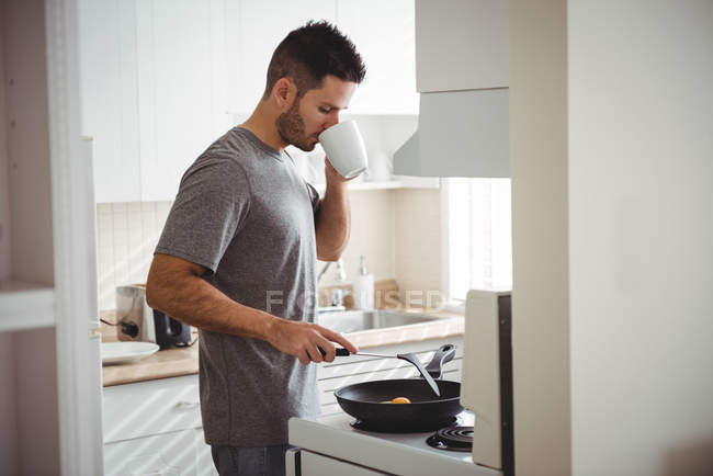 Человек пьет кофе во время приготовления пищи на кухне дома — стоковое фото