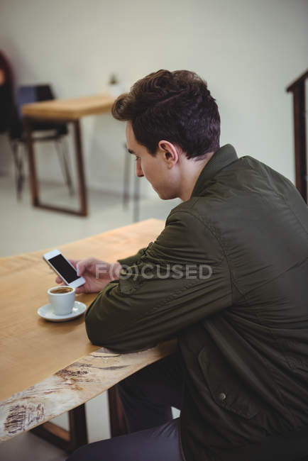 Vista lateral do homem usando seu telefone enquanto sentado em uma cafeteria — Fotografia de Stock