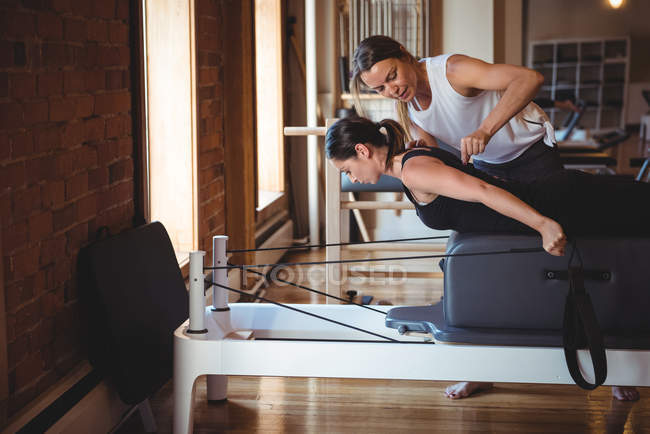 Entraîneur aidant une femme tout en pratiquant des pilates dans un studio de fitness — Photo de stock