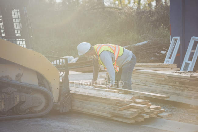 Construction worker loading timber on bulldozer at construction site — Stock Photo