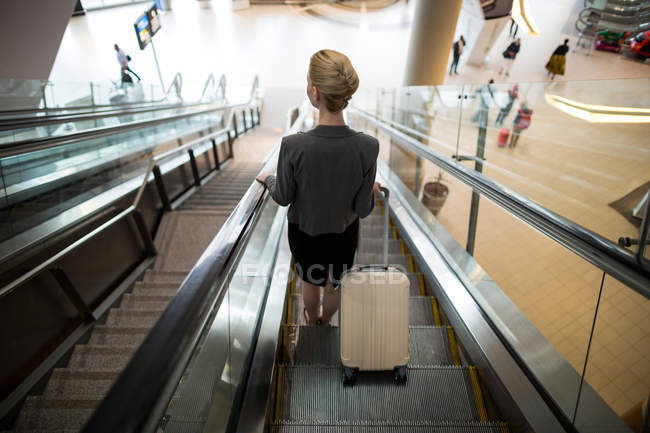 Vista traseira da empresária em pé na escada rolante com bagagem no aeroporto — Fotografia de Stock