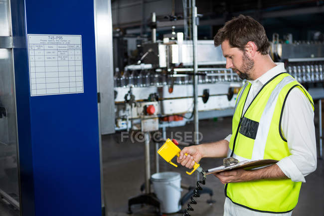 Vista lateral del trabajador masculino utilizando maquinaria en la fábrica de zumos - foto de stock