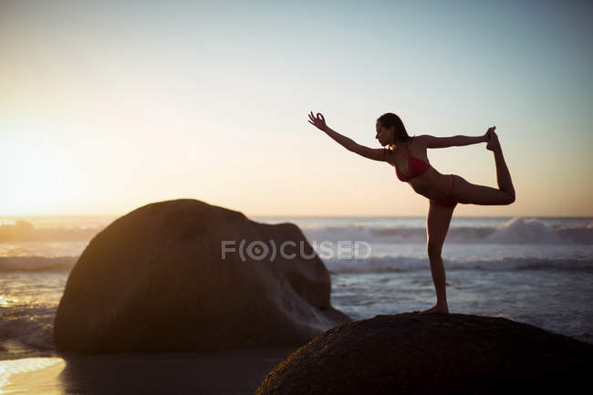 Mujer realizando ejercicio de estiramiento en la playa al atardecer - foto de stock