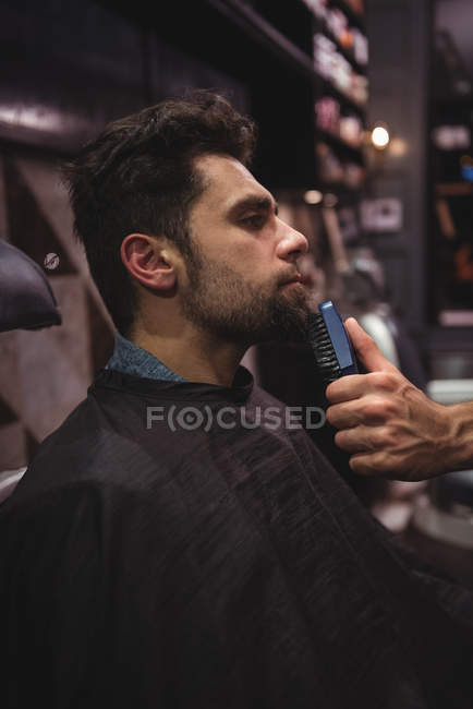 Homem recebendo barba raspada com aparador na barbearia — Fotografia de Stock