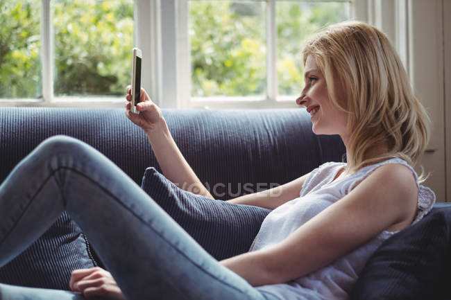 Женщина сидит на диване и пользуется мобильным телефоном в гостиной дома — стоковое фото