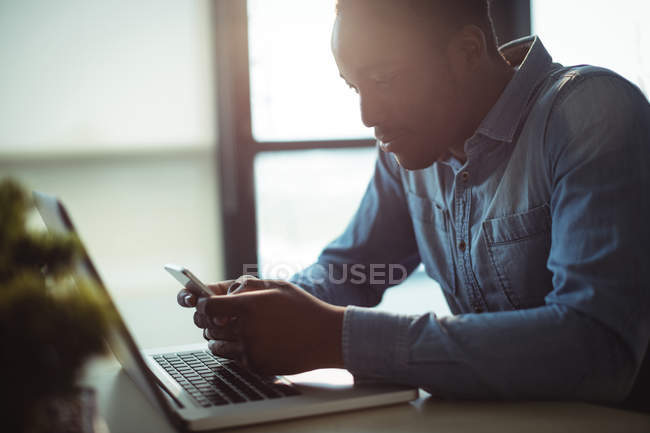 Männliche Führungskräfte nutzen Mobiltelefon, während sie im Büro am Laptop arbeiten — Stockfoto