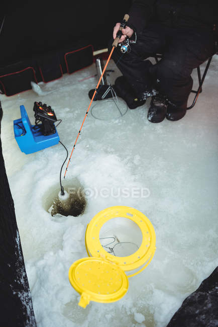 Sección media del pescador de hielo pescando mientras está sentado en la tienda - foto de stock