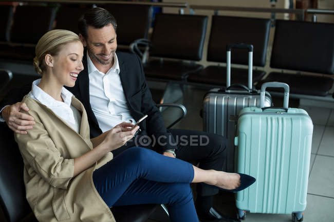 Casal feliz usando telefone celular no aeroporto — Fotografia de Stock