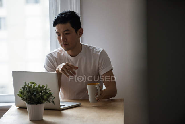 Чоловік дивиться на ноутбук, маючи чашку кави вдома — стокове фото