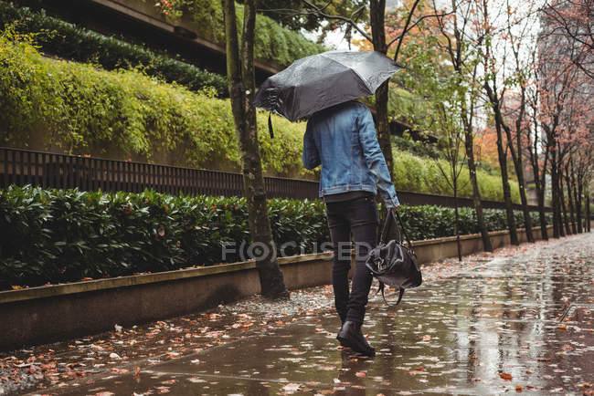 Вид сзади на человека с сумочкой и зонтиком, идущего по пешеходной дорожке — стоковое фото
