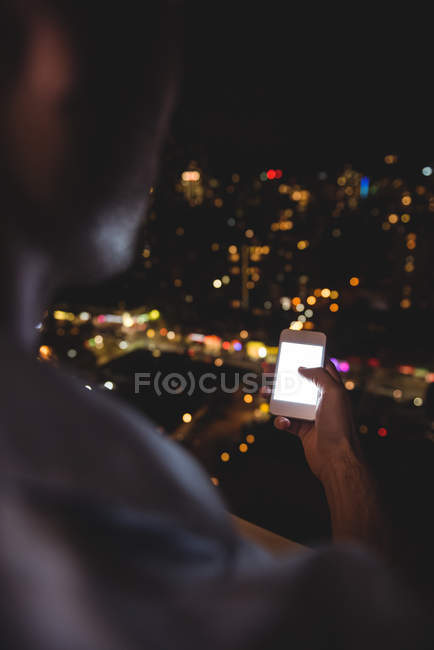 Visão traseira do homem usando seu telefone celular na varanda à noite — Fotografia de Stock
