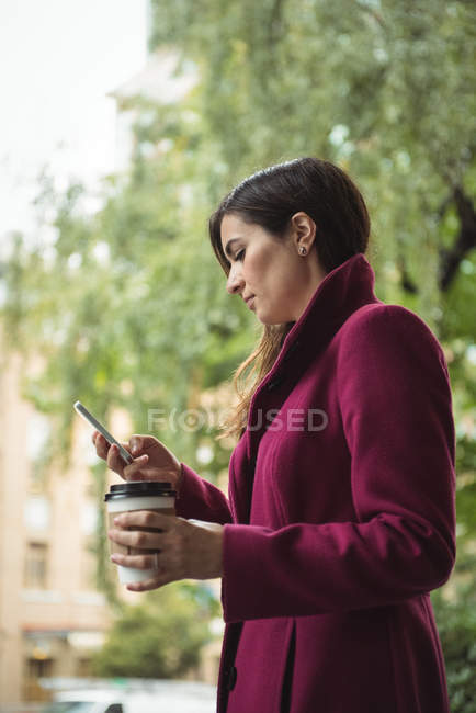 Деловая женщина с одноразовой чашкой кофе и мобильным телефоном на улице — стоковое фото