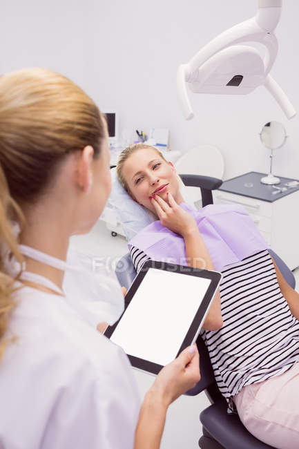 Доктор з цифровим планшетом розмовляє з пацієнткою з зубним болем у клініці — стокове фото
