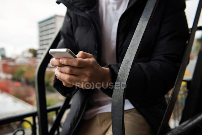 Средняя часть человека с помощью мобильного телефона на балконе — стоковое фото