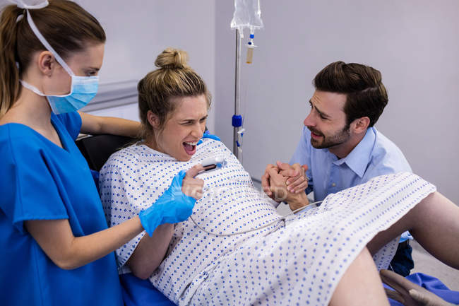 Médico examinando a una mujer embarazada durante el parto mientras el hombre sostiene su mano en el quirófano - foto de stock