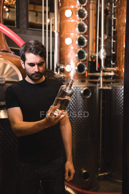 Hombre examinando una botella de alcohol en la fábrica de cerveza - foto de stock