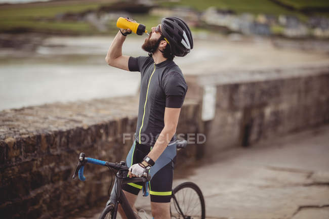 Atleta rinfrescante dalla bottiglia mentre guida in bicicletta su strada costiera — Foto stock