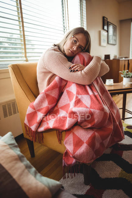 Nachdenkliche Frau sitzt und umarmt Knie im Wohnzimmer zu Hause — Stockfoto