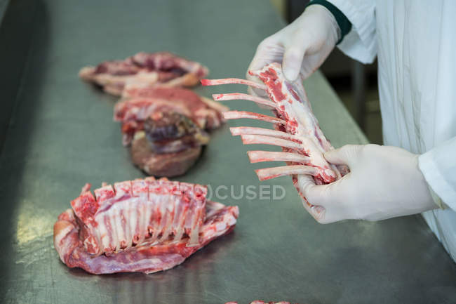 Primer plano del carnicero que sostiene la carne de costillas en la fábrica de carne - foto de stock