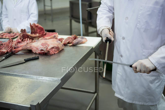 Carniceiro afiando faca na fábrica de carne — Fotografia de Stock