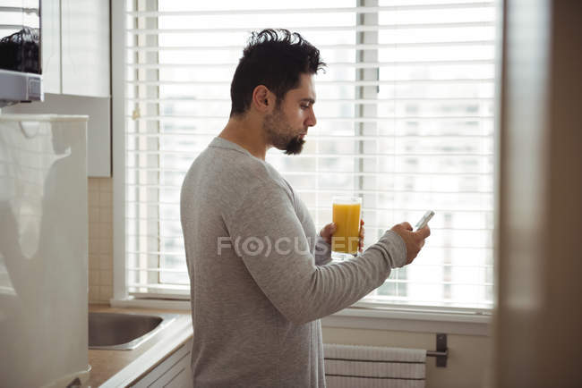 Mann benutzt Handy, während er Saft in der Küche zu Hause hat — Stockfoto