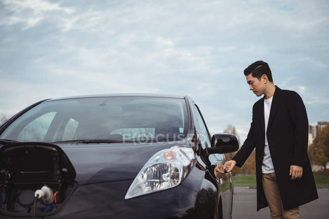 Homme ouvrant la porte de la voiture électrique à la station de recharge du véhicule électrique — Photo de stock