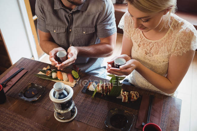 Casal tendo sake enquanto come sushi no restaurante — Fotografia de Stock