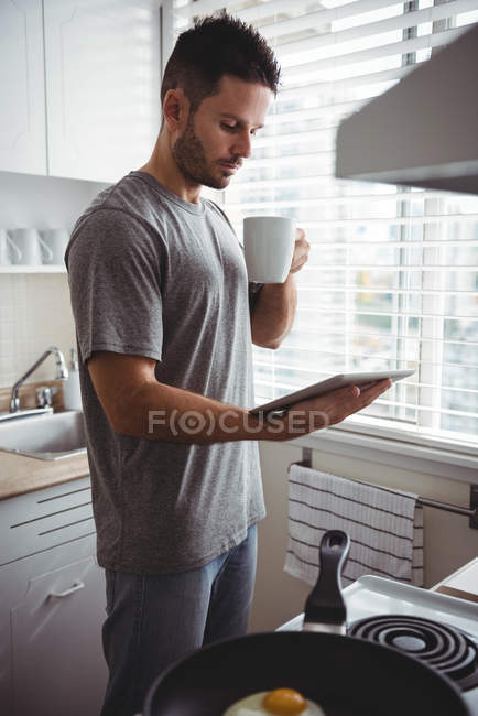 Людина використовує цифровий планшет, маючи каву на кухні вдома — стокове фото
