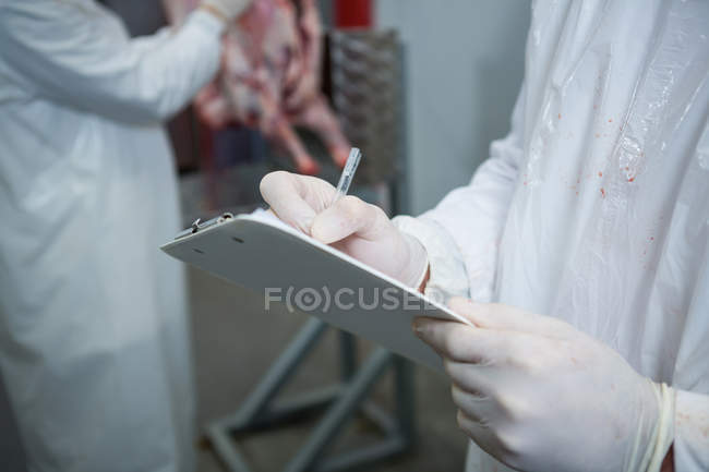 Sección media del carnicero sujetando el portapapeles en la fábrica de carne - foto de stock