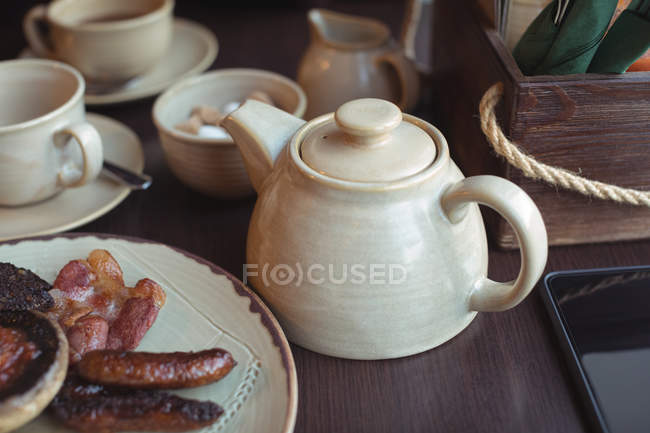 Close up of teapot and plate of English breakfast on table in cafe — Stock Photo