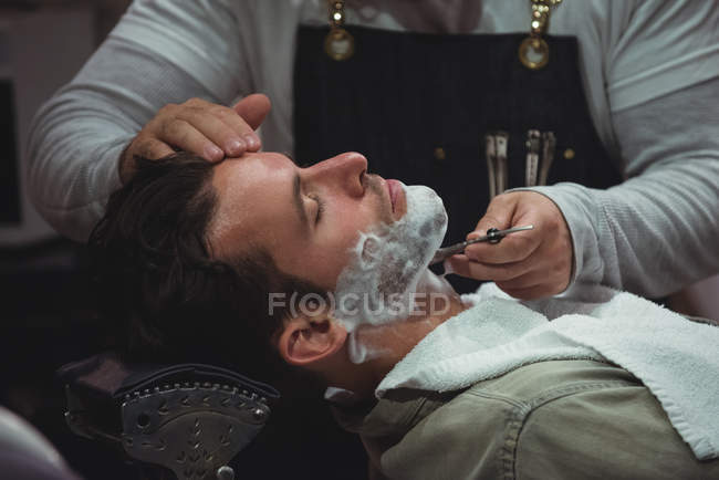 Client getting beard shaved with razor in barber shop — Stock Photo