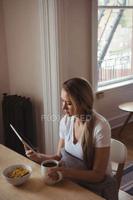 Donna che usa tablet digitale mentre fa colazione a casa — Foto stock