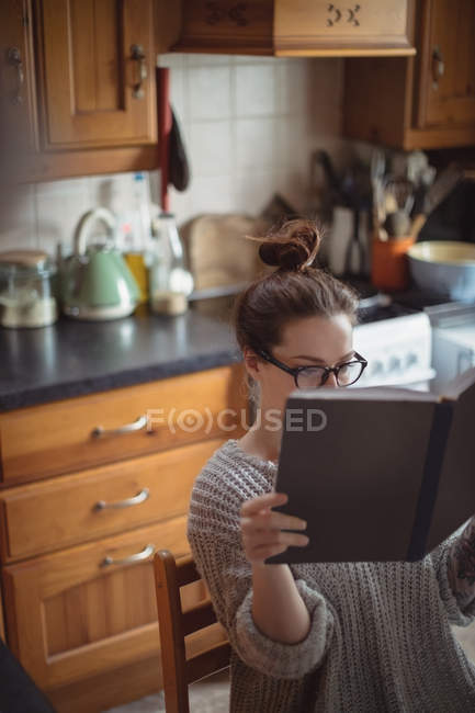 Mujer leyendo libro en cocina en casa - foto de stock