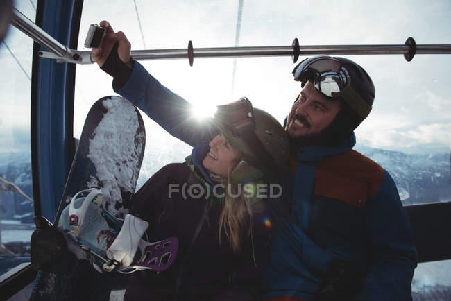 Couple heureux prenant selfie dans le téléphérique aérien contre le ciel pendant l'hiver — Photo de stock