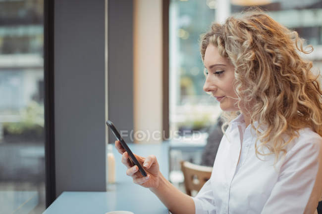 Vista lateral de la mujer de negocios sentada con smartphone en el mostrador en la cafetería - foto de stock