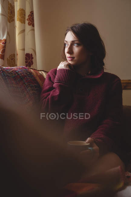 Thoughtful woman sitting and holding a coffee cup at home — Stock Photo