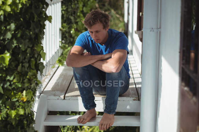 Занепокоєний чоловік сидить з обіймами, схрещеними на ганку — стокове фото