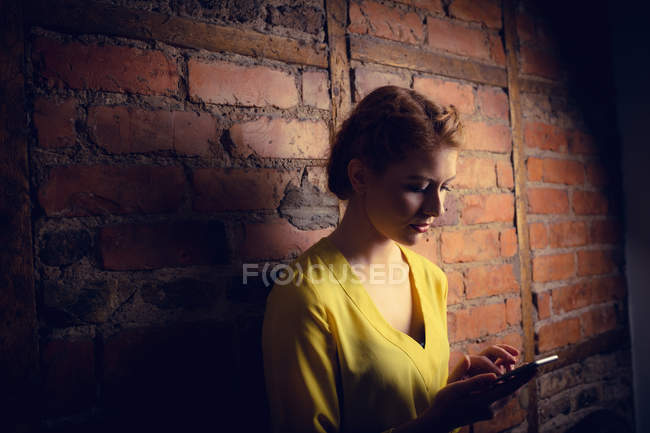 Donna in piedi contro muro di mattoni e utilizzando il telefono cellulare — Foto stock