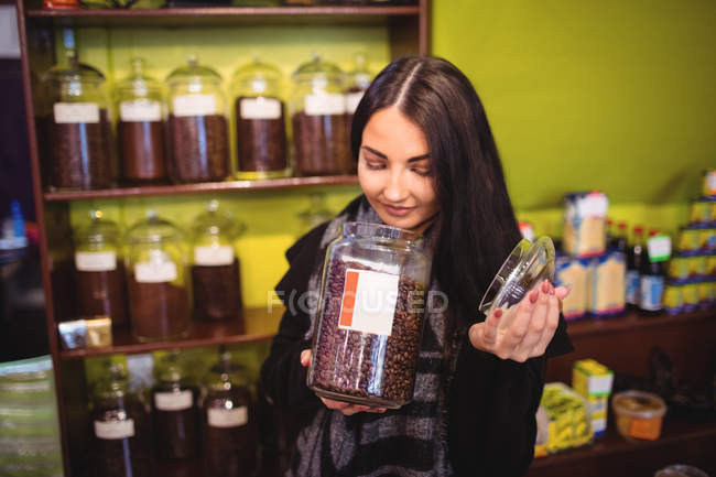 Mulher bonita cheirando frasco de grãos de café na loja — Fotografia de Stock