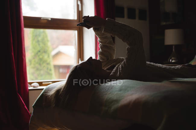 Mulher deitada e usando telefone celular na cama no quarto — Fotografia de Stock