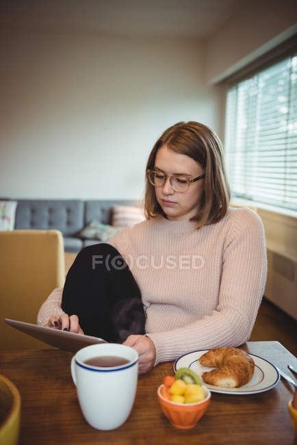 Frau nutzt digitales Tablet beim Frühstück im heimischen Wohnzimmer — Stockfoto
