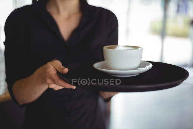 Section médiane de serveuse debout avec une tasse de café dans le café — Photo de stock