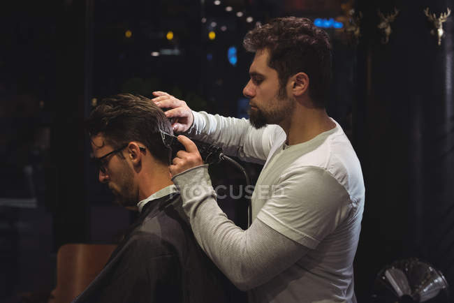 Man getting hair trimmed by hairdresser with trimmer in barber shop — Stock Photo