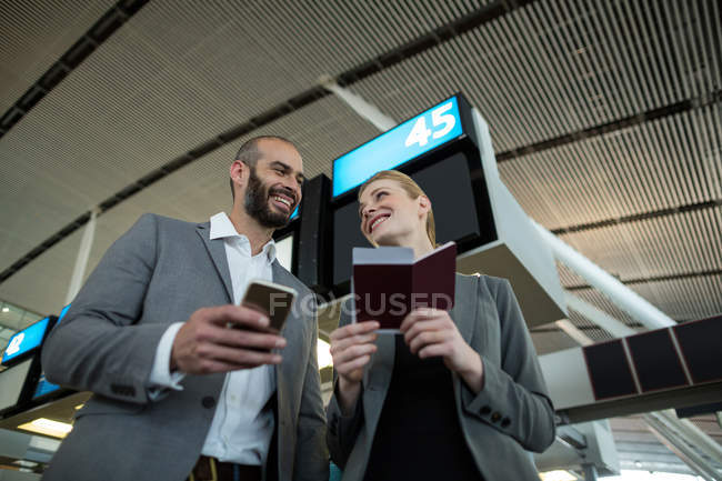 Gente de negocios con tarjeta de embarque y teléfono móvil en la terminal del aeropuerto - foto de stock