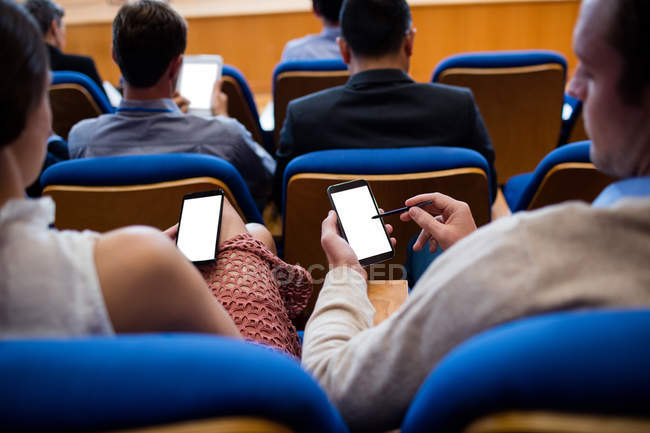 Ejecutivos de negocios que participan en una reunión de negocios con teléfono móvil en el centro de conferencias - foto de stock